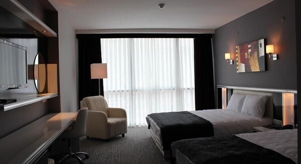 A hotel room with a bed, a desk, a chair, a TV, and a large window with curtains. - Cavusoglu Tower Hotel (Tokat)