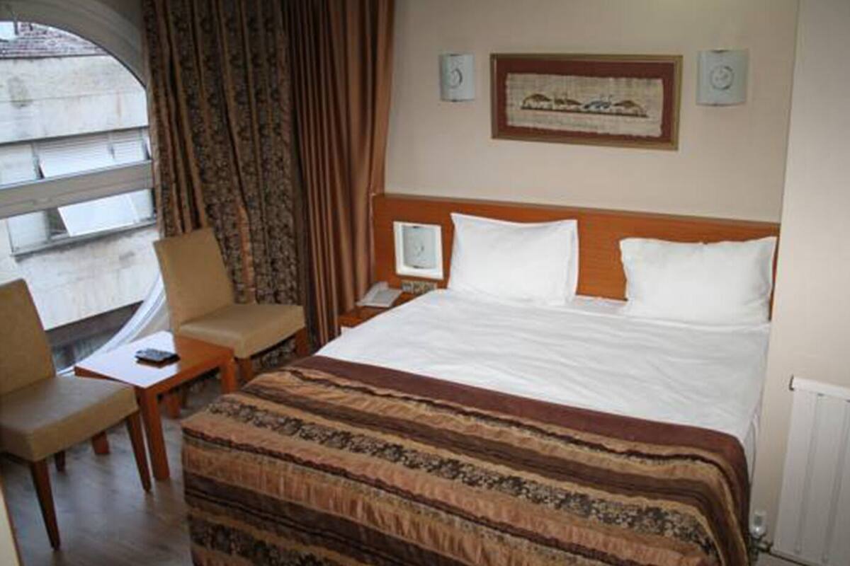 Une chambre d’hôtel avec un lit, une chaise, un bureau et une fenêtre avec des rideaux.