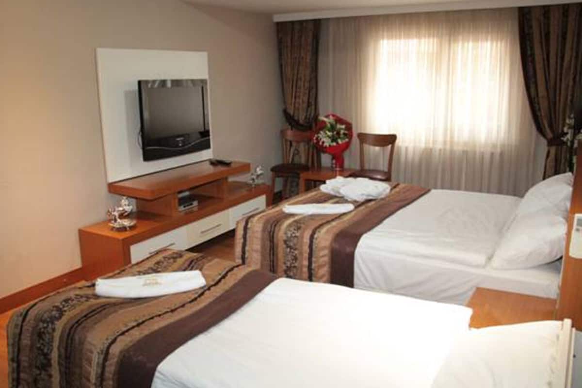 Une chambre d’hôtel avec deux lits, un téléviseur posé sur un meuble en bois, un bureau et une chaise.