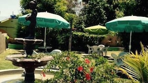 Un jardín con una fuente, sombrillas verdes y abundante follaje.