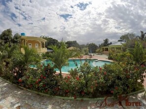 A pool area with a clear view of a building in the background. - La Cayenna Hôtel et Restaurant (Port-au-Prince)