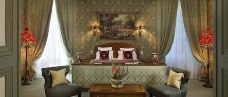 A bedroom with a large bed, two armchairs, a wooden coffee table, and a painting on the wall.