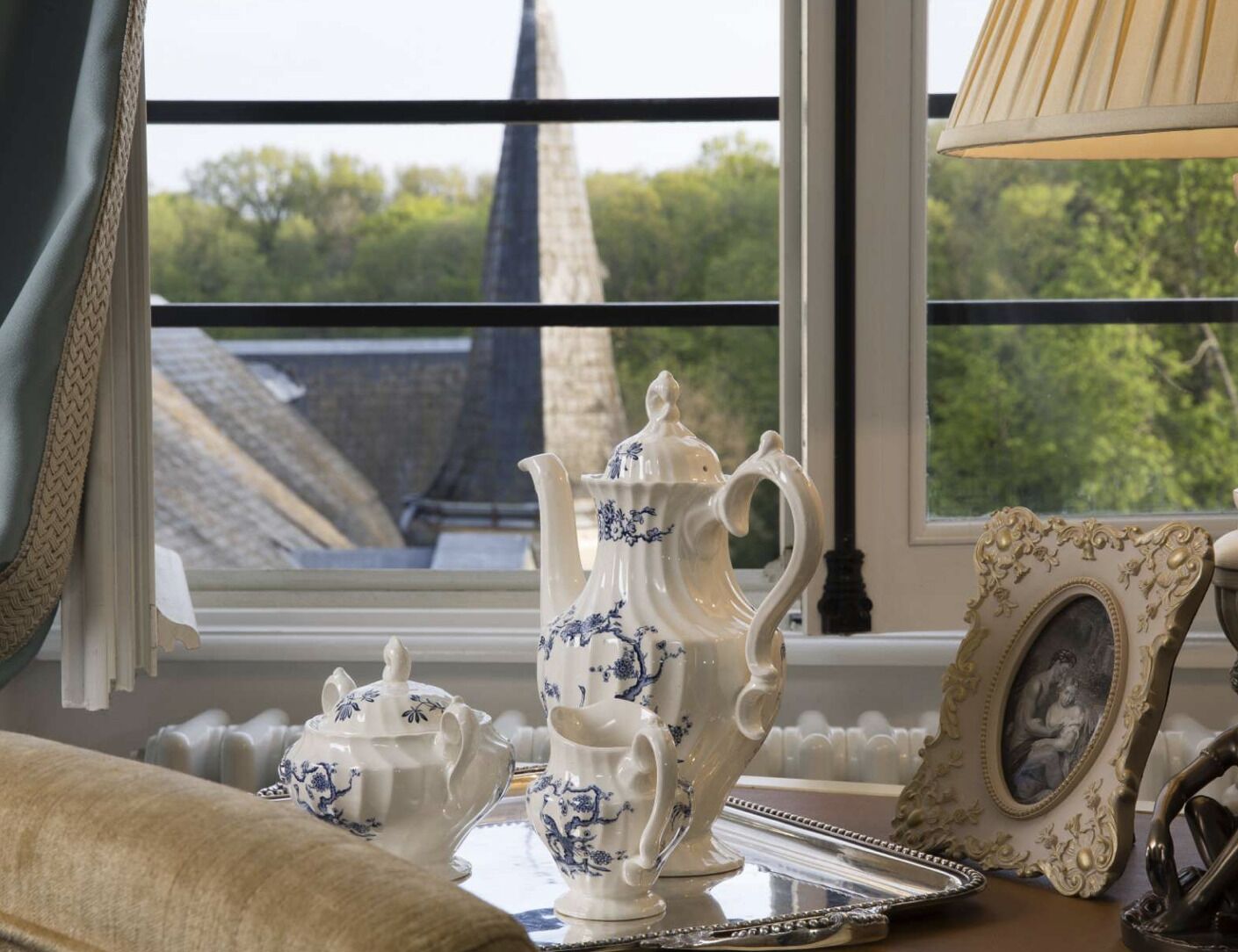 A table set with white porcelain tea service, a framed picture, and a lamp.