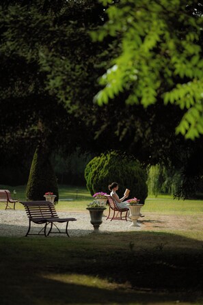 A park with benches, a woman reading, and a well-maintained garden. - Château Laroche Ploquin, The Originals Relais (Sepmes)