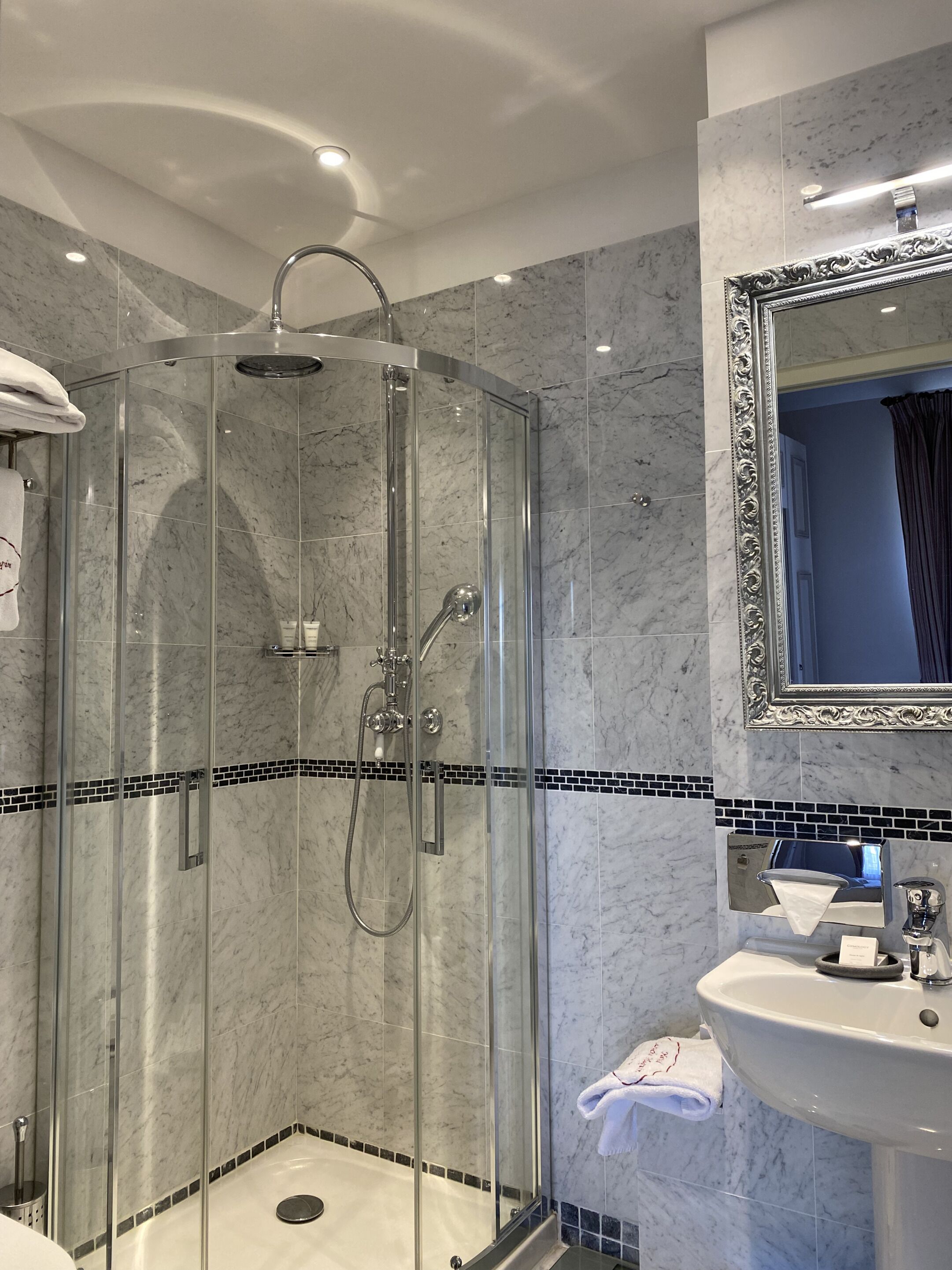 Een moderne badkamer met een douchecabine van glas, een wand betegeld met marmer en een wastafel met spiegel.
