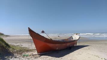 A boat on a sandy beach with the ocean in the background.