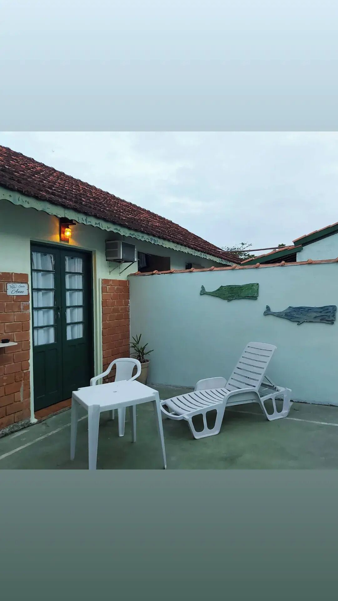 Un pequeño espacio al aire libre con una puerta verde, una silla blanca y una tumbona.
