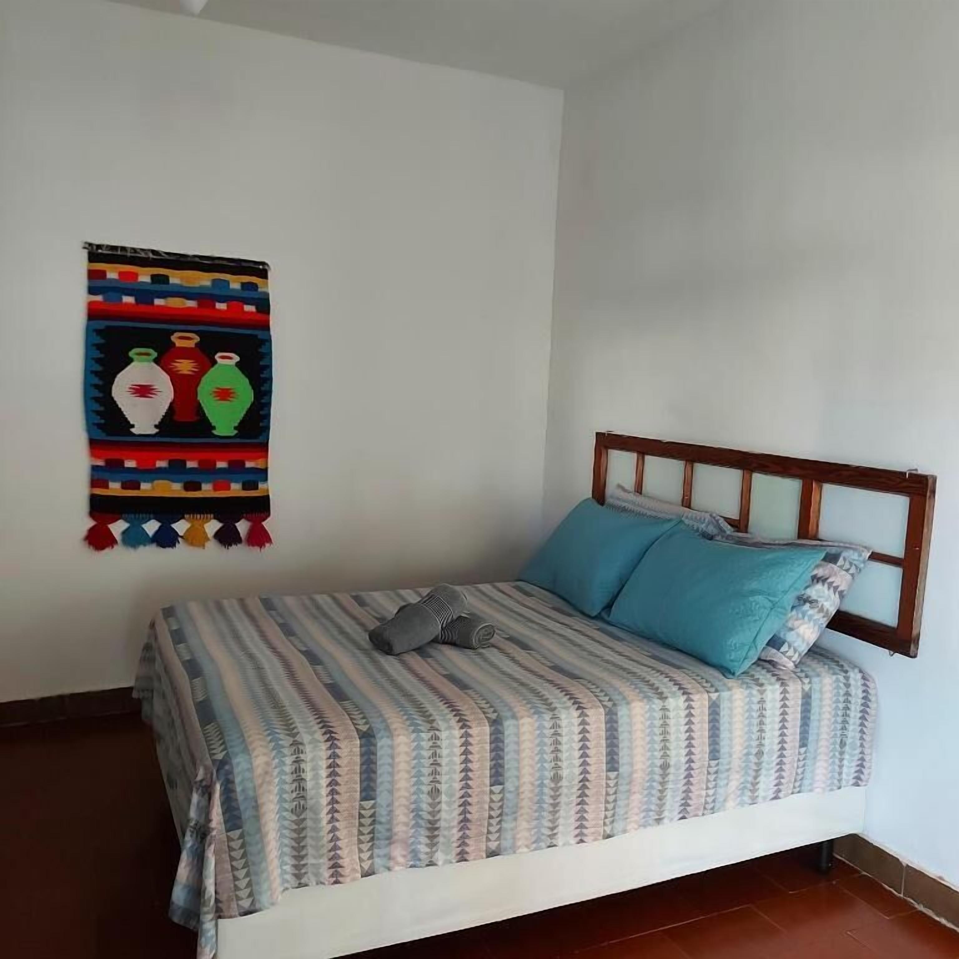 Una cama con colcha a rayas y dos almohadas, un cabecero de madera y un adorno de pared con jarrones de colores.