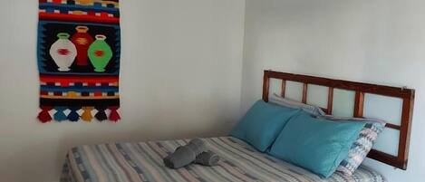 Una cama con colcha a rayas y dos almohadas, un cabecero de madera y un adorno de pared con jarrones de colores.