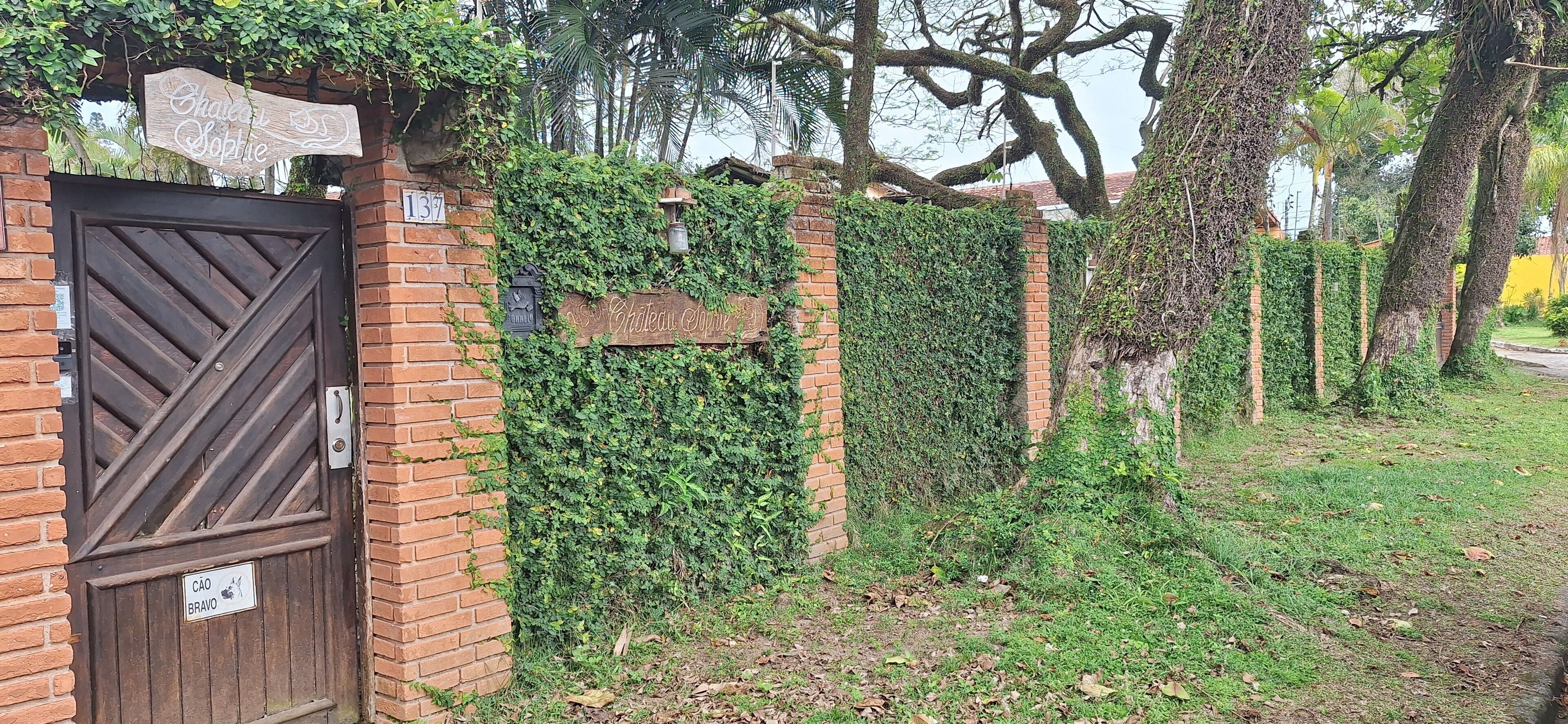 A gated entrance with a wooden sign, brick wall, and greenery.
