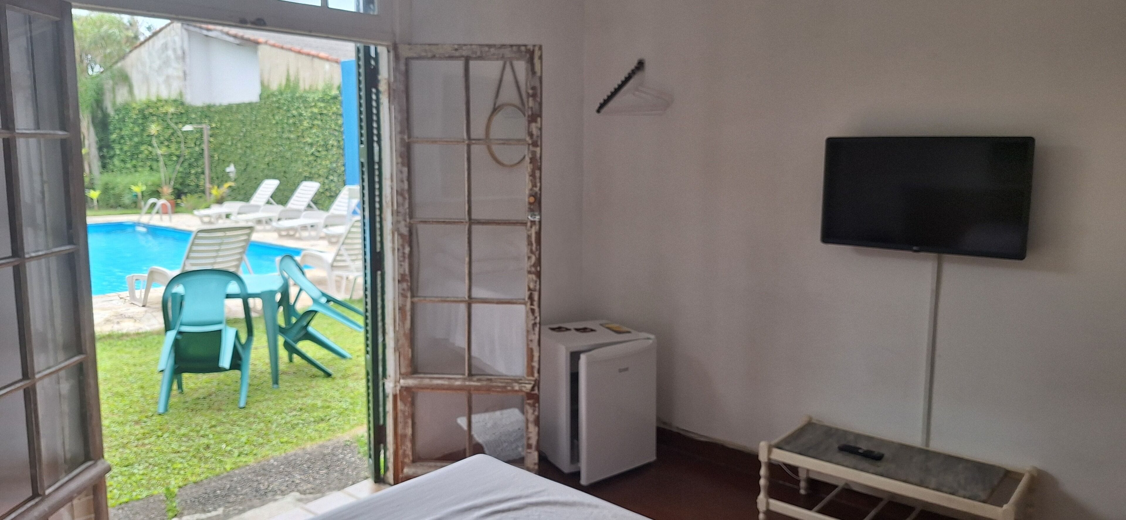 Una habitación con cama, televisión instalada en la pared, una mesita y vistas a una piscina con sillones de descanso al aire libre.