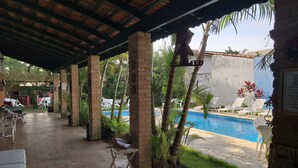 A covered outdoor area with a pool, lounge chairs, and a brick wall. - Pousada Chateau Sophie (Itanhaém)