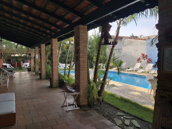Un espacio al aire libre techado con piscina, sillas de descanso y un muro de ladrillo.