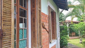 Un edificio con fachada de ladrillo, contraventanas de madera y un pequeño jardín con un banco.