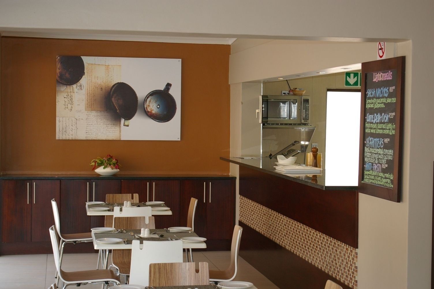 A restaurant with a counter, menu board, and dining area with chairs and tables.