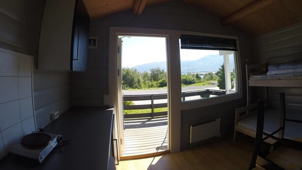 Habitación compacta con techo de madera, ventana con vistas a la vegetación y montañas, una litera y una pequeña zona de kitchenette.