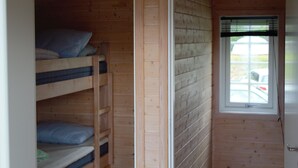 Una habitación con paredes de madera, una cama litera, una ventana con persianas y una puerta.