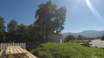 Una mesa de picnic y bancos en un área con césped, con montañas al fondo.