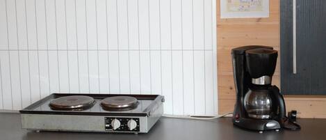 A kitchenette with a stove, a coffee maker, and a white refrigerator.