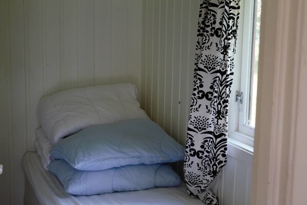 Una cama con almohadas blancas y azules, una ventana con cortina estampada y una pared blanca con líneas verticales.
