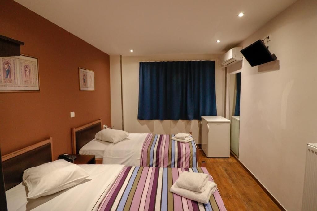 A hotel room with two beds, a television mounted on the wall, and a window with blue curtains.