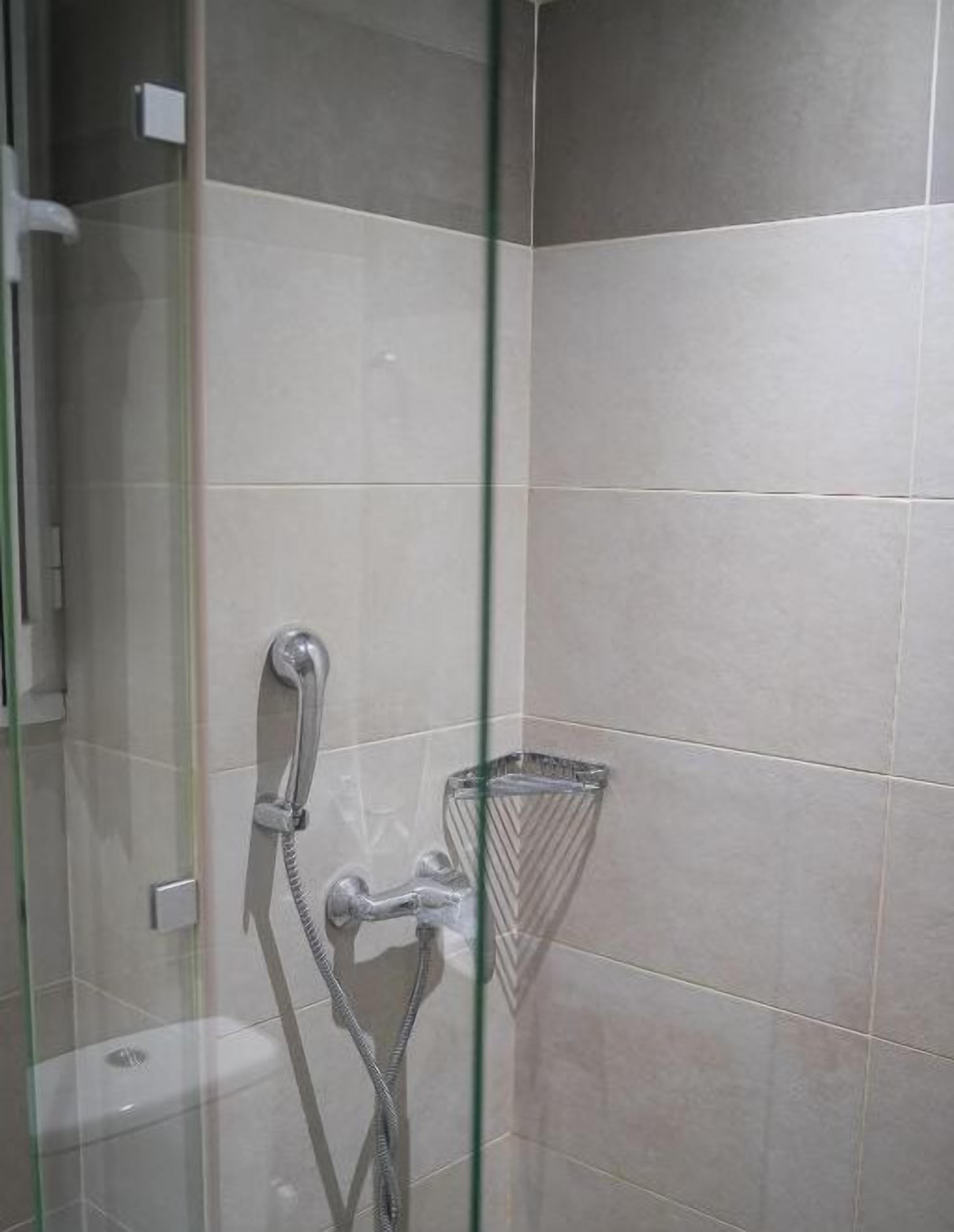 Un espacio de ducha con puerta de vidrio, cabezal de ducha de mano y plato de ducha de vidrio.