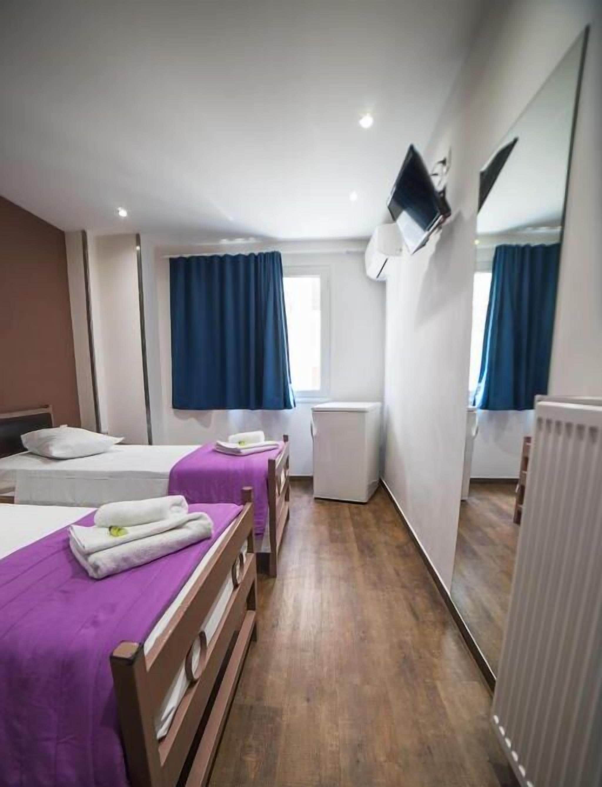 Una camera d'albergo con due letti, una piccola scrivania, uno specchio e una finestra con tende.