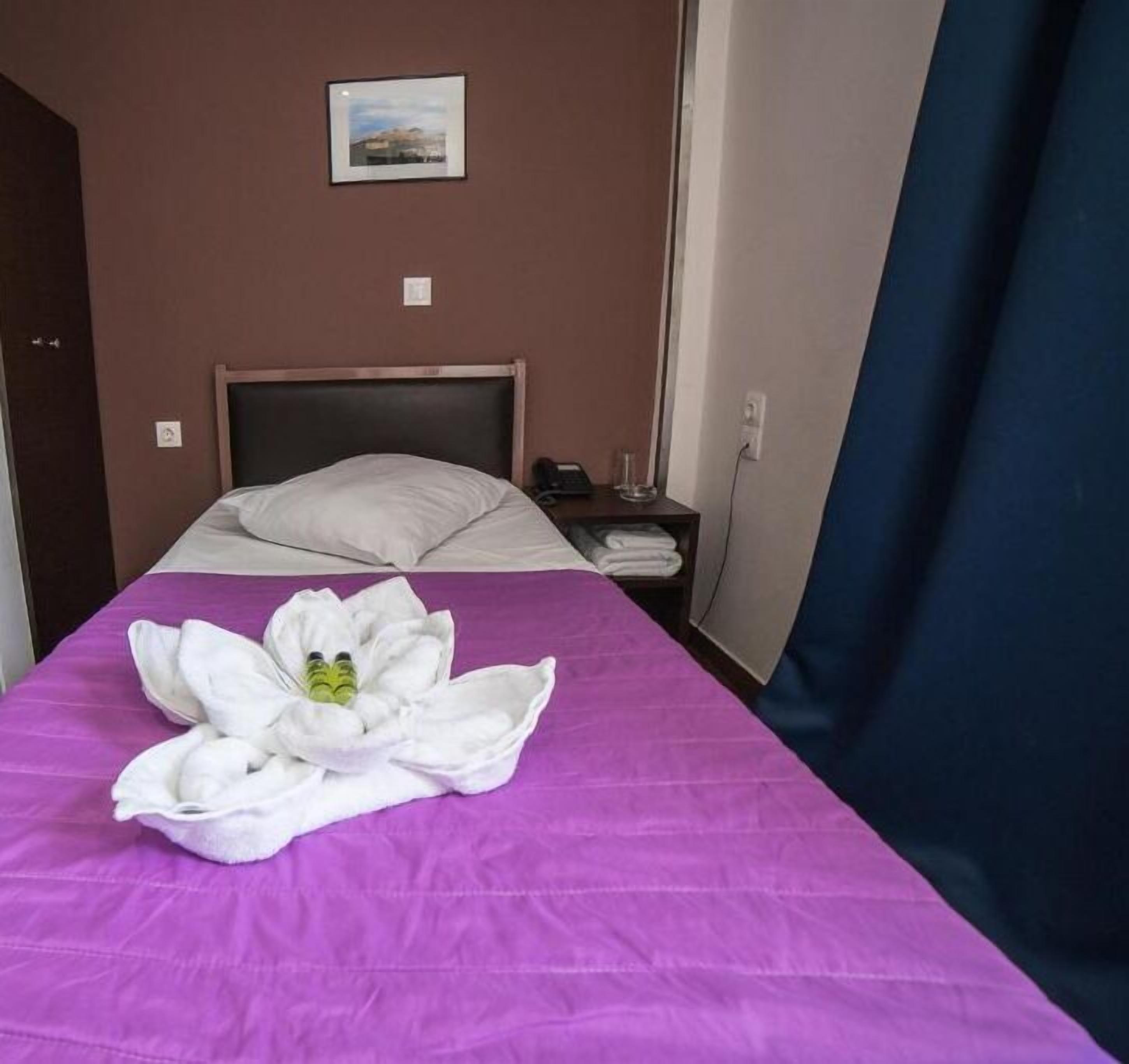 A hotel room with a bed, a nightstand, a lamp, and a picture on the wall.