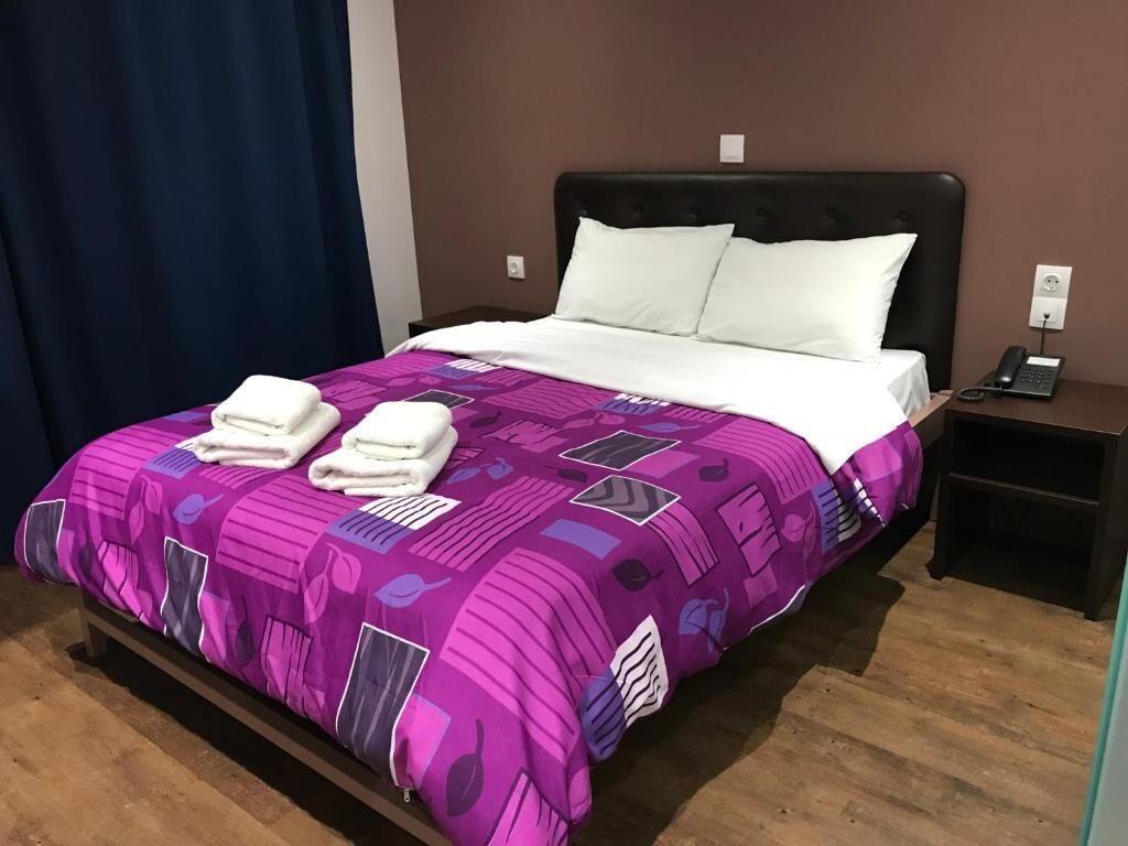 Una cama bien hecha con una colcha morada y blanca estampada, dos almohadas blancas y dos toallas blancas dobladas sobre la cama.