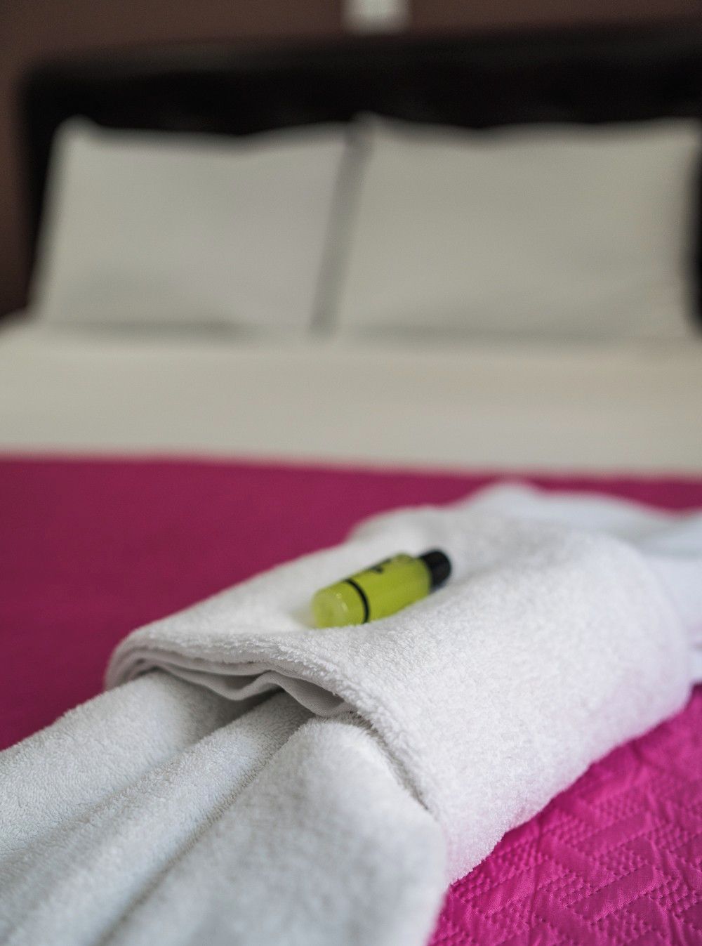 A neatly folded white towel with a green object on it, placed on a pink surface.
