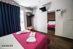A hotel room with a bed, a TV, a mirror, an air conditioning unit, and a window with curtains. - Mansion Hotel  (Athens)