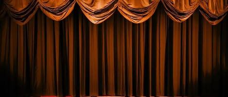 A theater stage with a dark curtain backdrop and a seated audience.