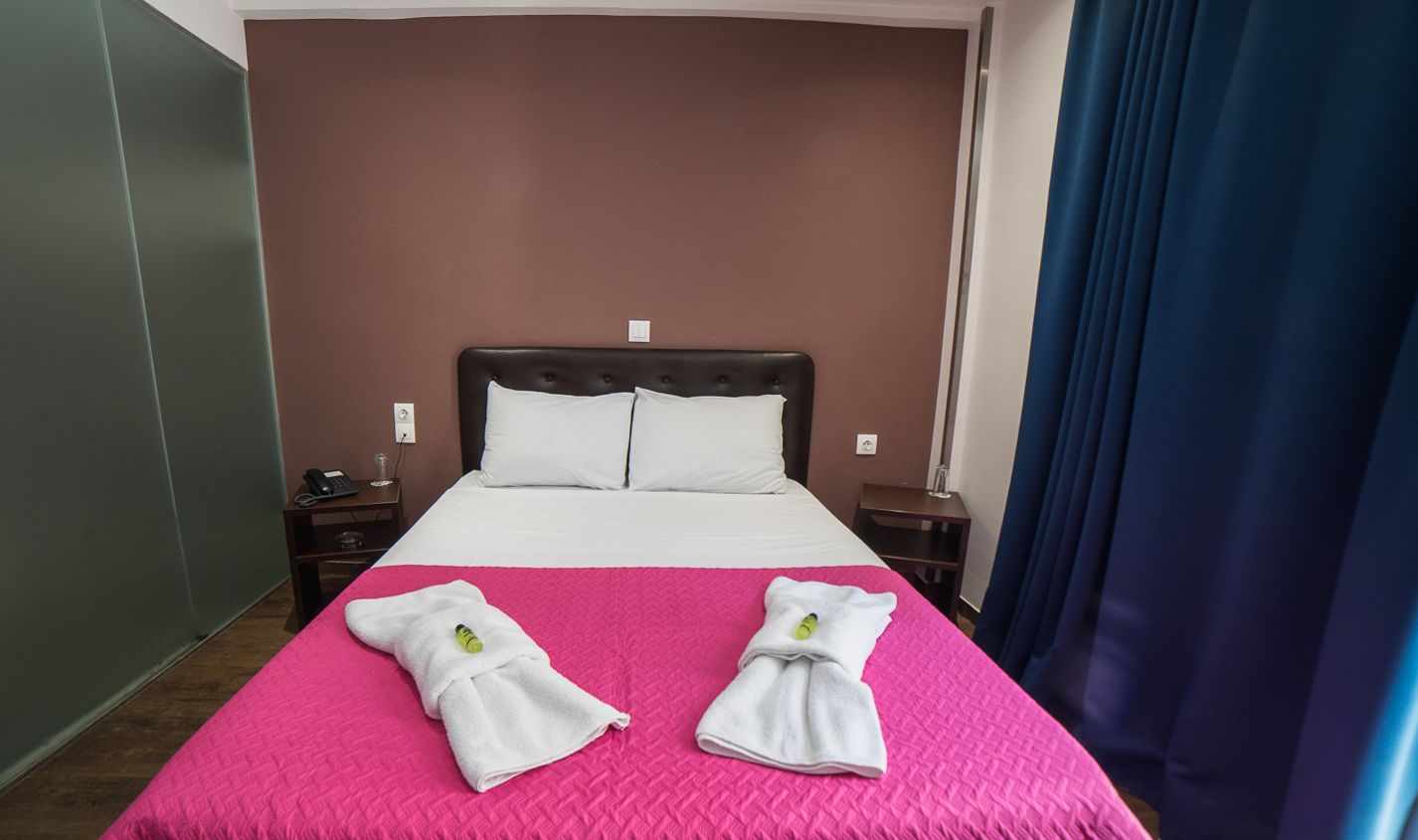 A hotel room with a bed, two nightstands, a blue curtain, and a pink bedspread.