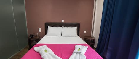 A hotel room with a bed, two nightstands, a blue curtain, and a pink bedspread.