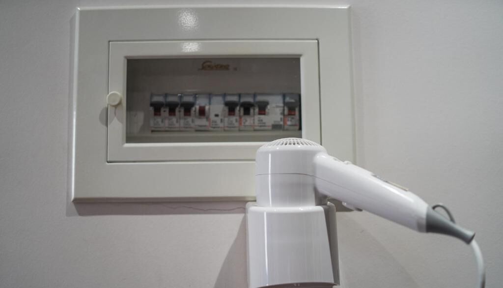 A white hair dryer mounted on a wall with a framed electrical outlet box above it.