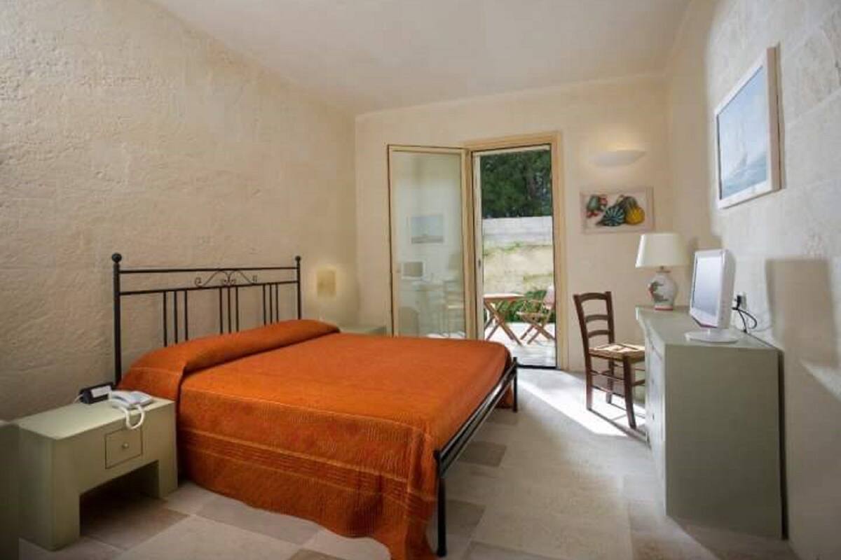 Un dormitorio con cama, escritorio con ordenador, silla y una pequeña mesa con lámpara.