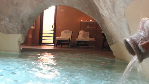 An indoor pool area with a stone archway, two lounge chairs, and a small table with a towel.