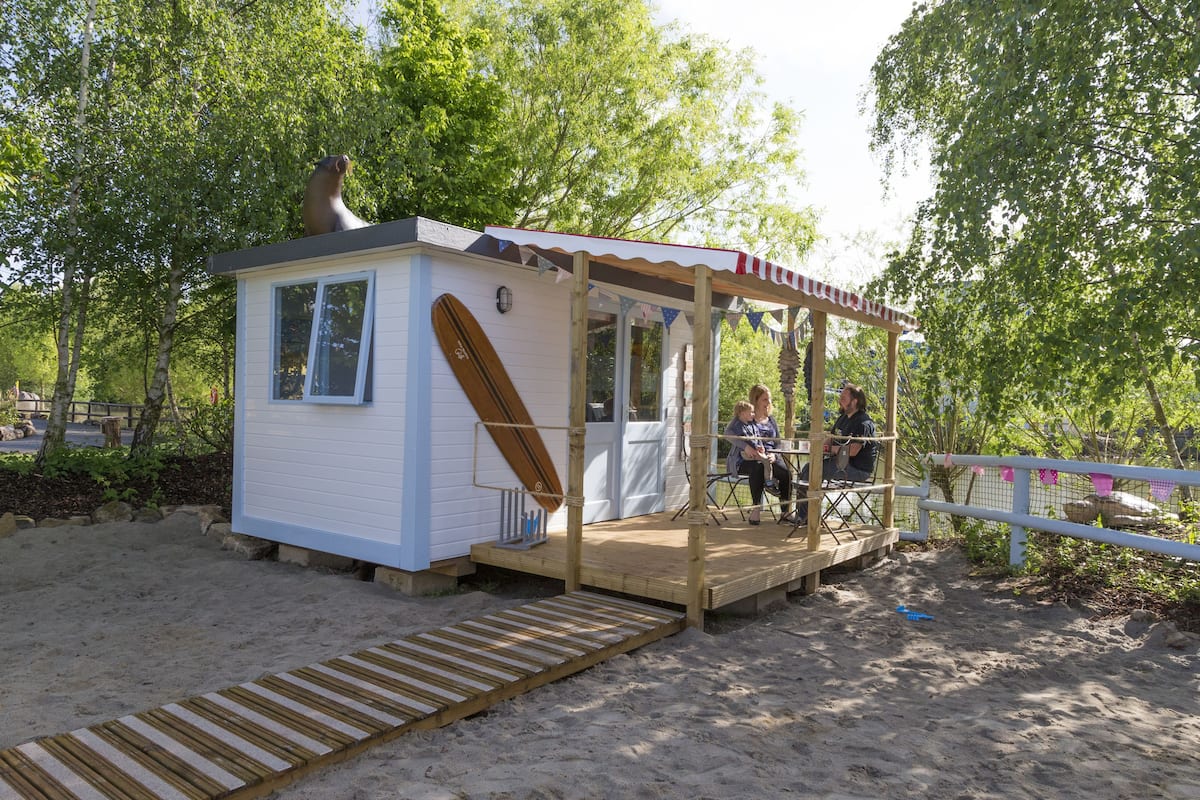 Une petite cabane située au bord de la plage, dotée d’une terrasse en bois, d’une seule fenêtre et d’un petit espace porche.