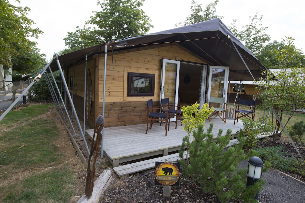 Une cabane en bois avec une terrasse, un panneau d’avertissement sur la présence d’ours et un petit jardin.
