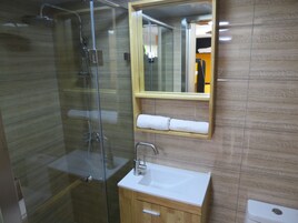 Un baño moderno con ducha envuelta en vidrio, tocador de madera con lavamanos y espejo sobre el tocador.