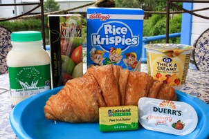 Una bandeja con un croissant, mantequilla de Lakeland dairies, mermelada de fresa Duerr's, una caja de Kellogg's Rice Krispies, una botella de jugo de manzana y una caja de yogur espeso y cremoso.