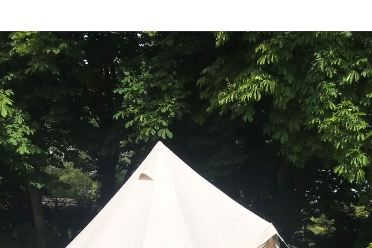 Une tente blanche avec une porte, installée sur un champ herbeux, avec des arbres en arrière-plan.