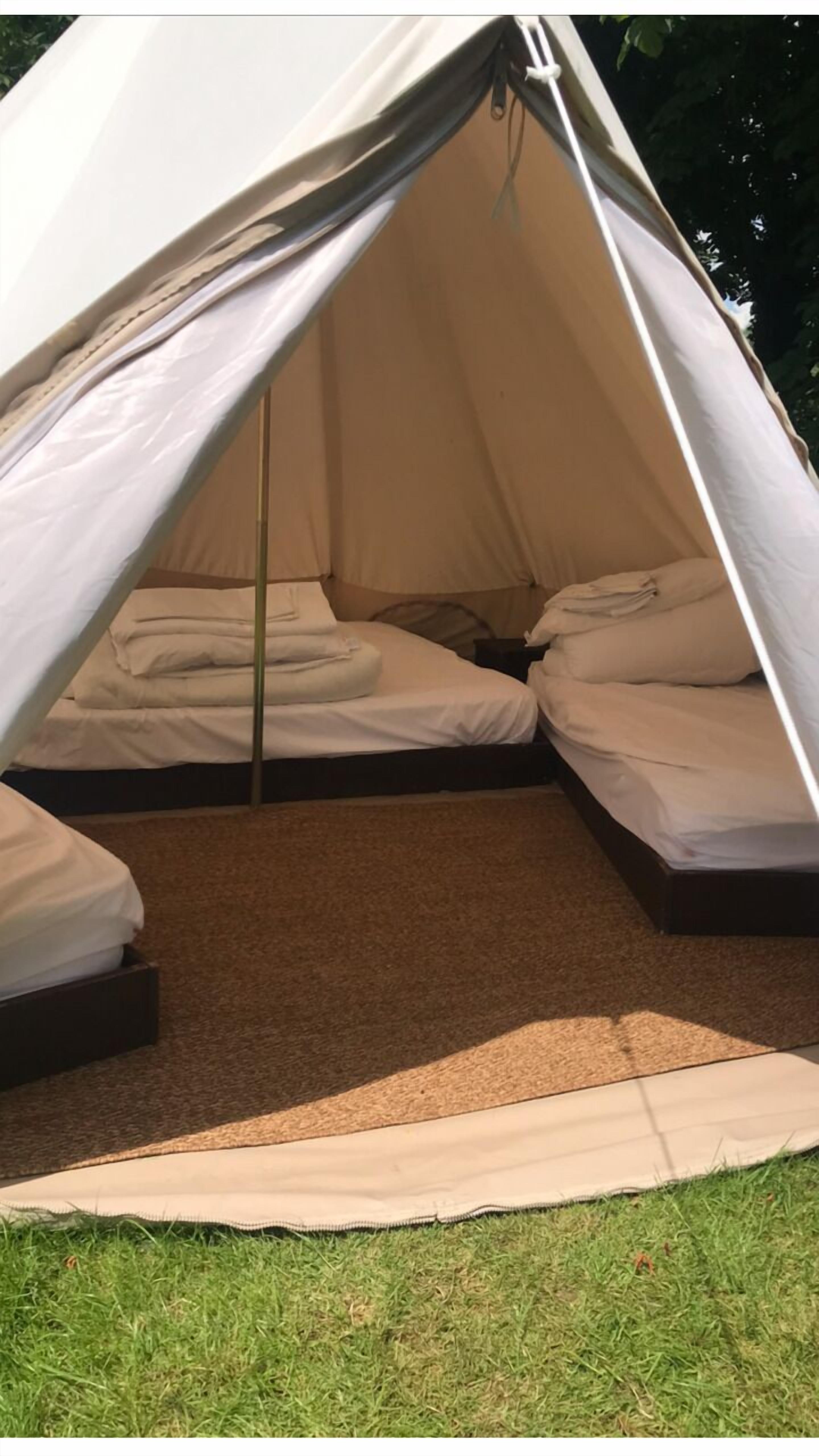 A tent with two beds, a central pole, and a grassy area outside.