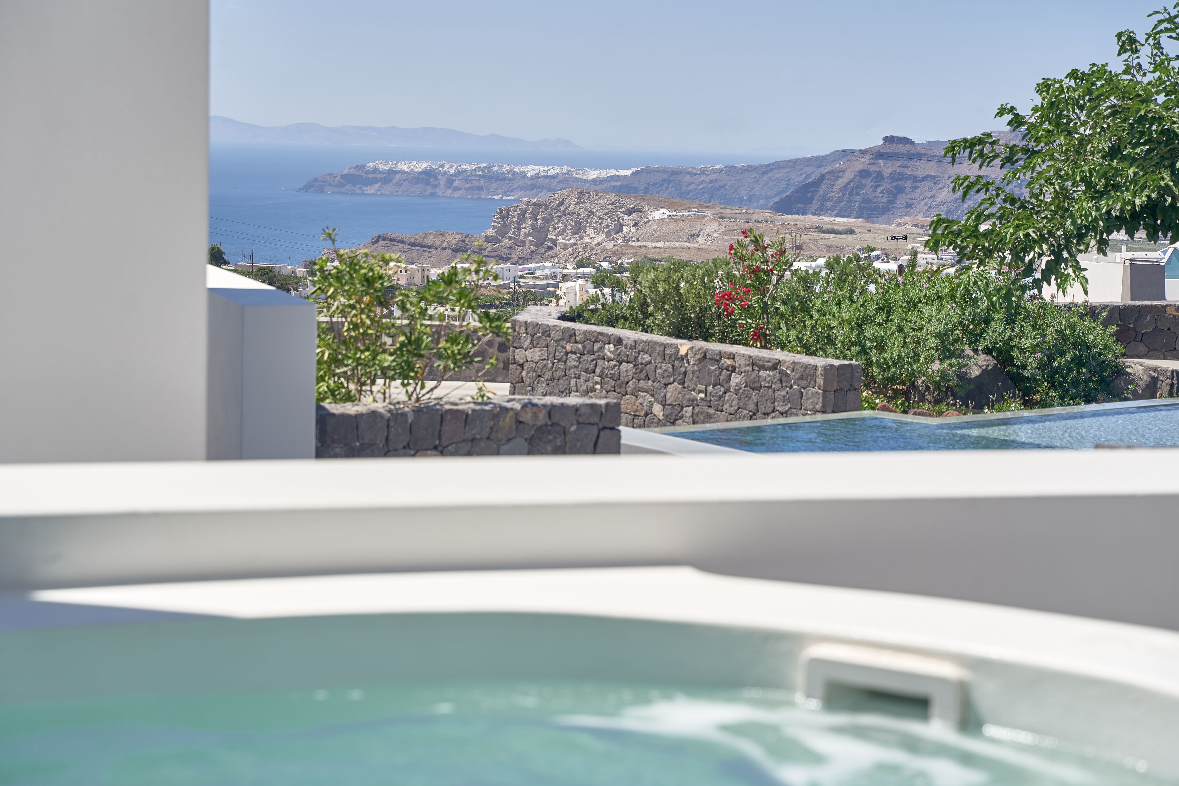 A modern hotel with a pool, stone walls, and a view of the sea and mountains.