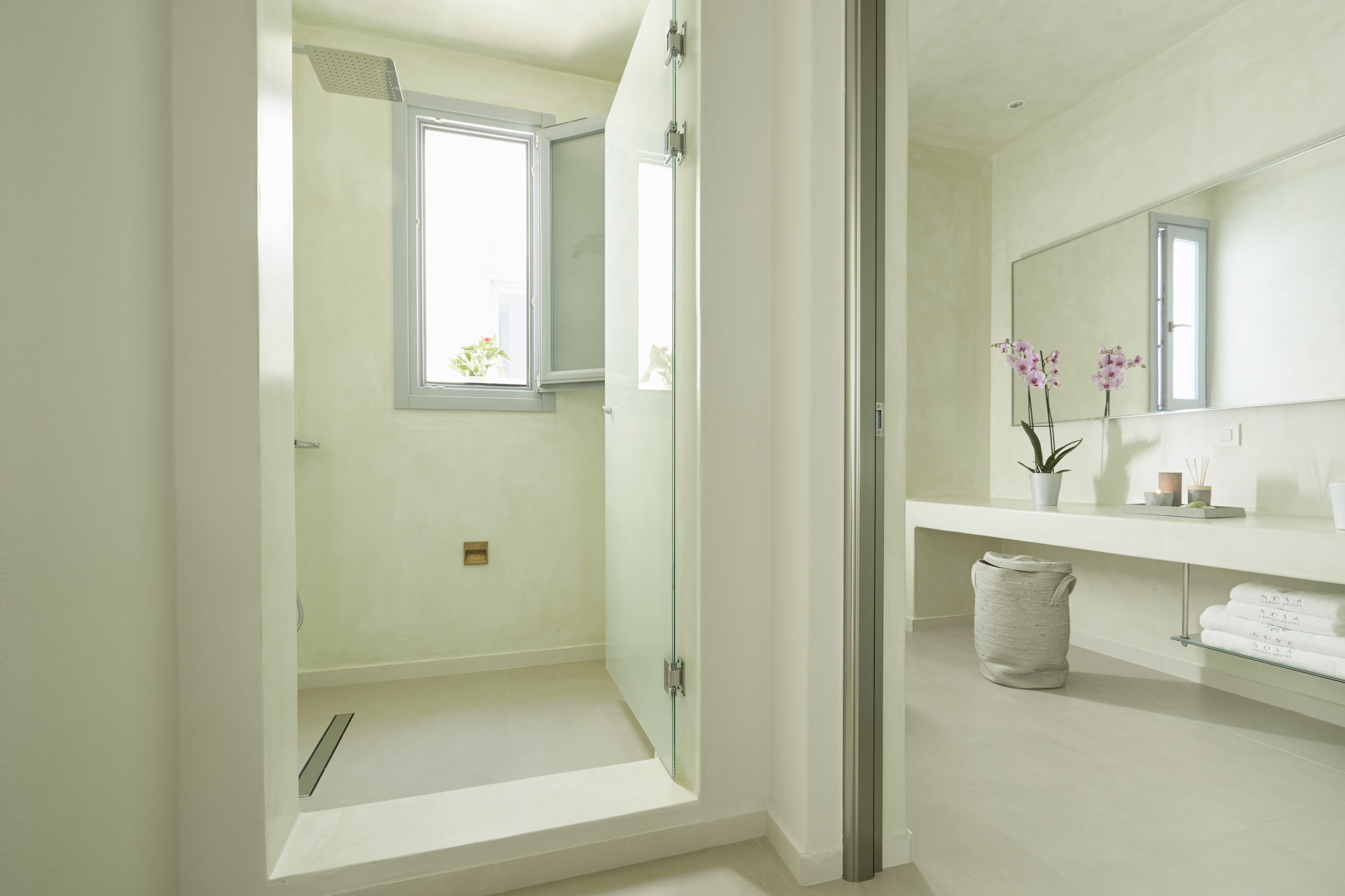 Un baño moderno con cabina de ducha de vidrio, un espejo grande y una ventana con vistas a la vegetación.
