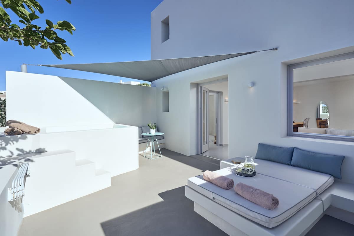Un espacio exterior moderno y minimalista con un sofá blanco, una mesita y un vaso de agua.