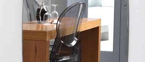A modern dining area with a wooden table and two transparent chairs, a glass vase, and a wine glass.