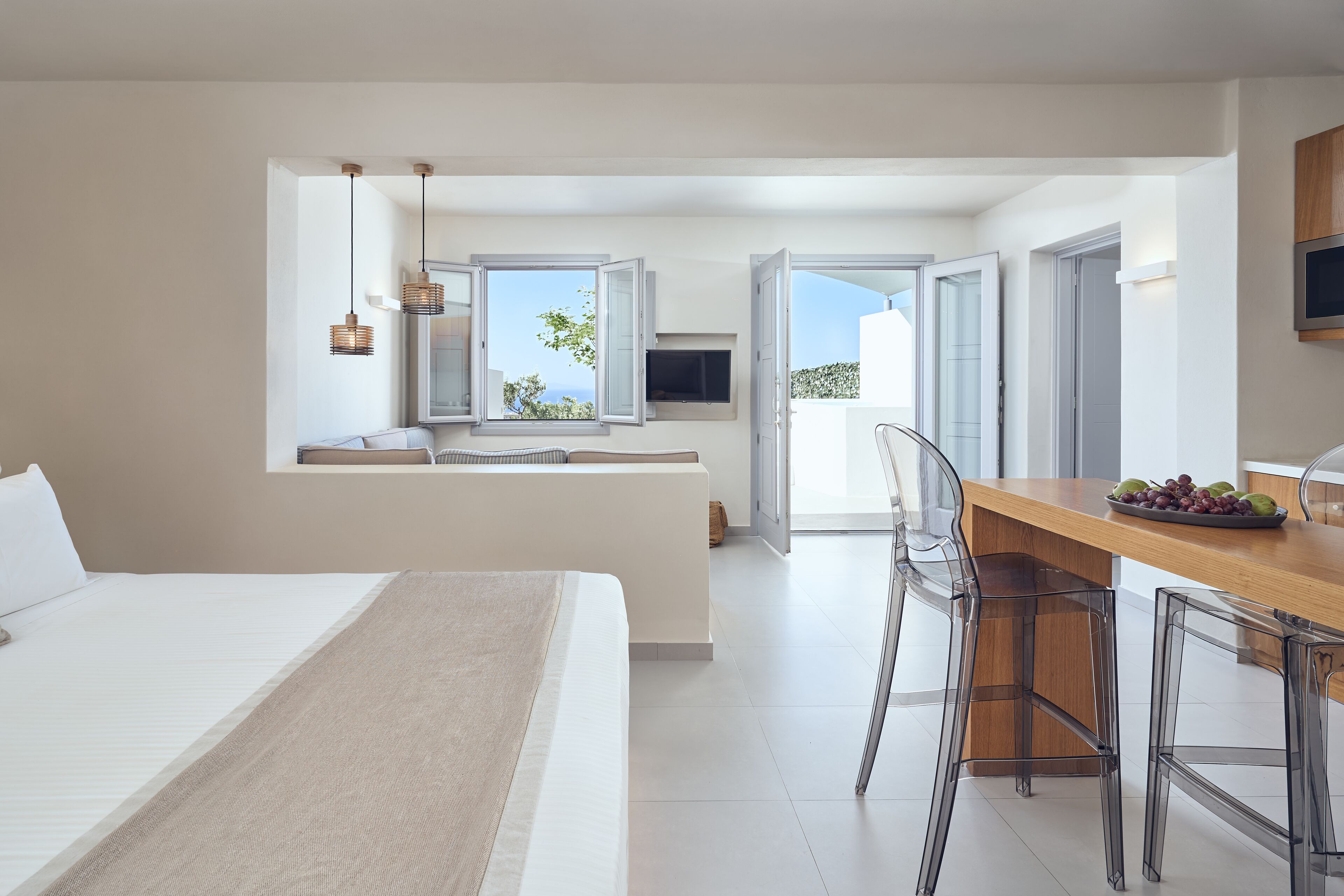 Una habitación de hotel moderna con una cama grande, una zona de comedor con una mesa y sillas de madera, un televisor y vistas al mar.