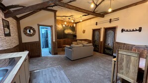 Un intérieur rustique avec des poutres apparentes, un mur en pierre, une cuisine moderne, un coin salon avec un canapé et une salle de douche.