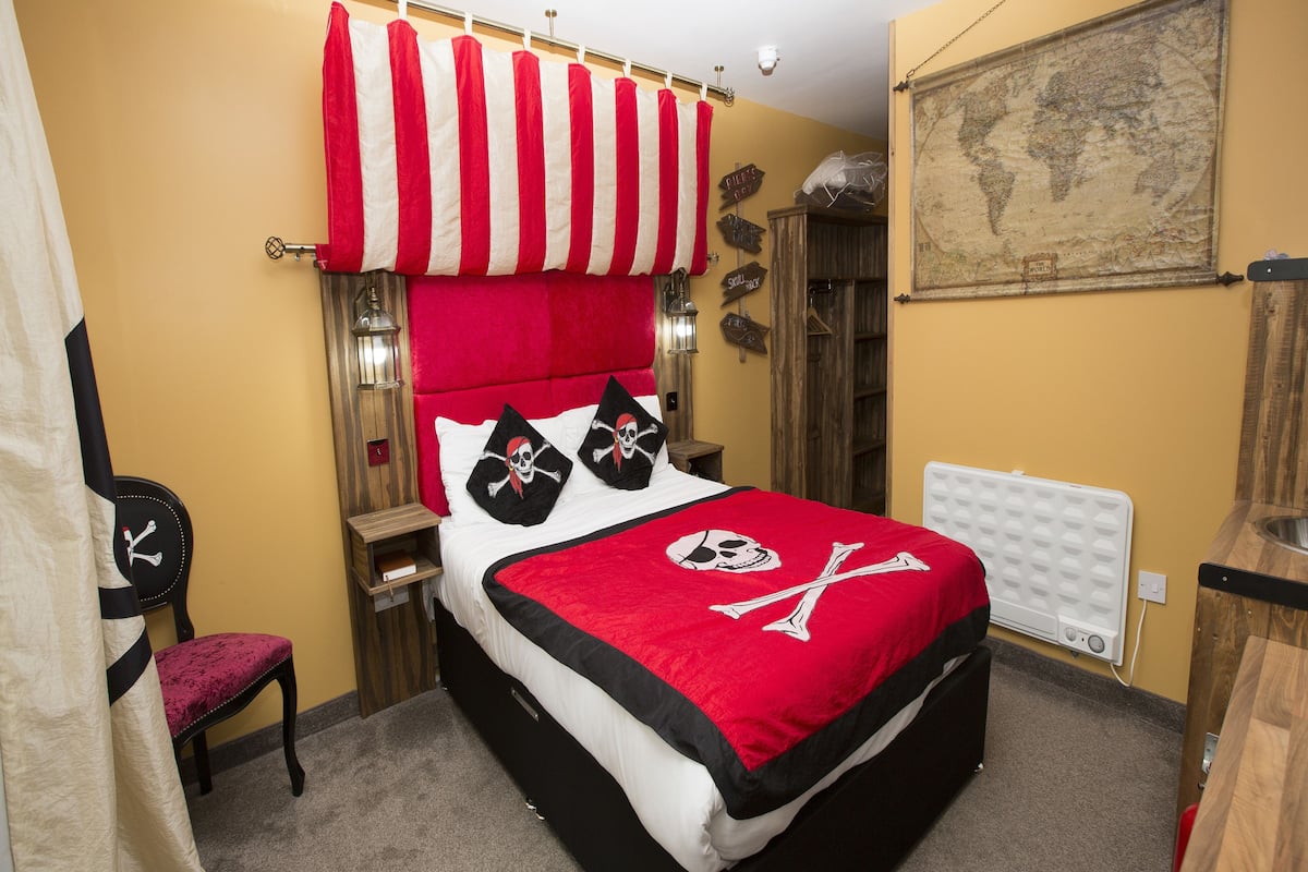 A bedroom with a bed, a chair, a map on the wall, and a window with curtains.